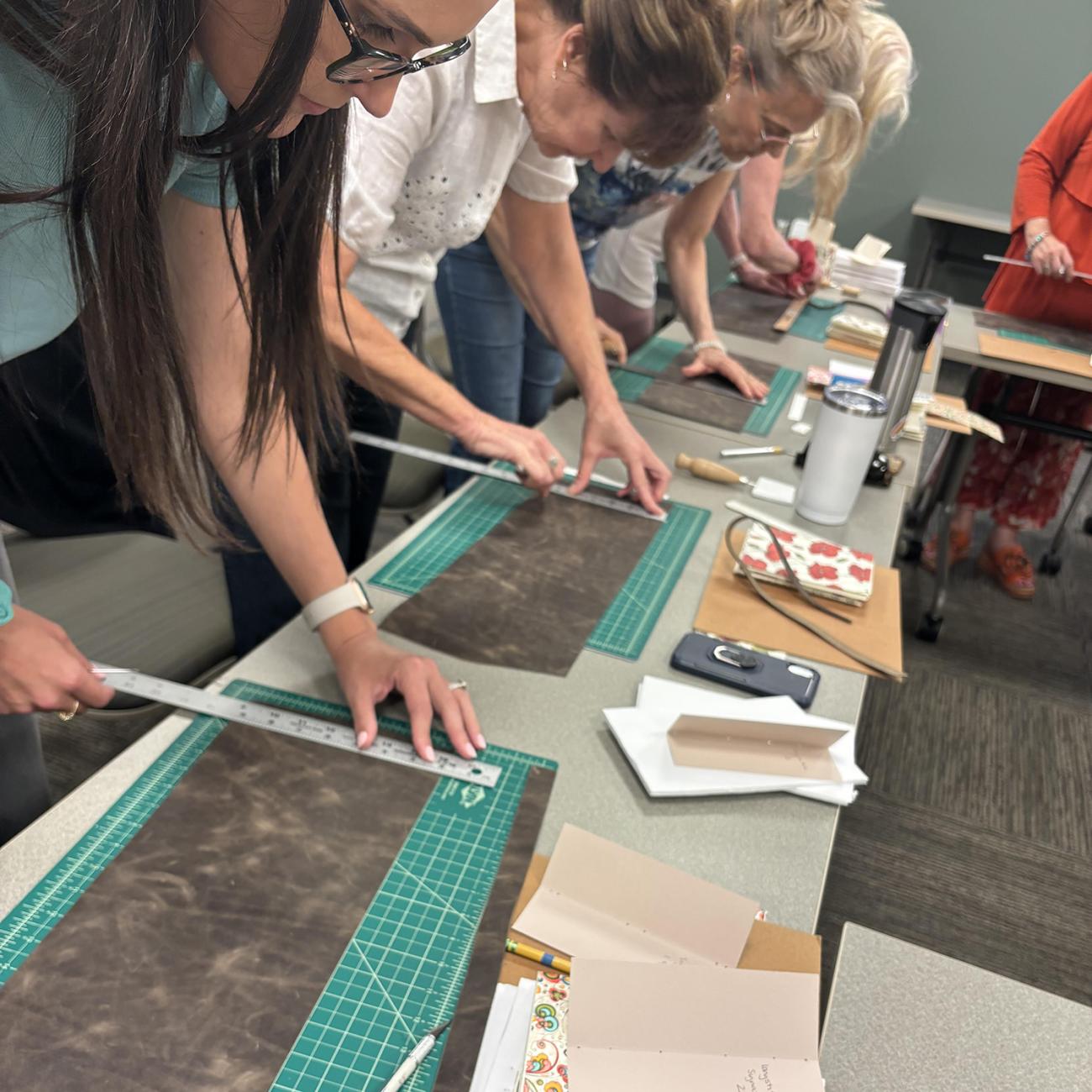 Women in a workshop measuring leather for a journal craft project