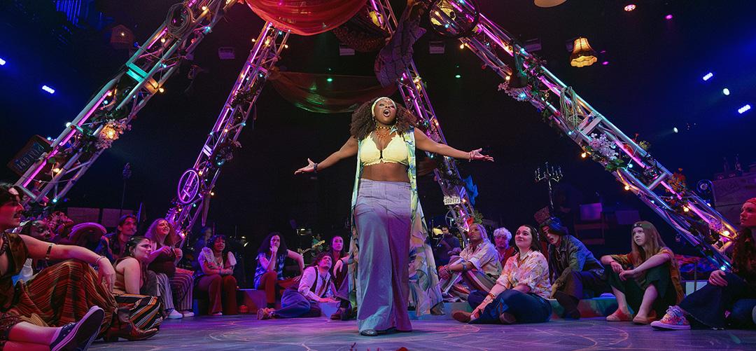 Actor in middle of stage surrounded by cast