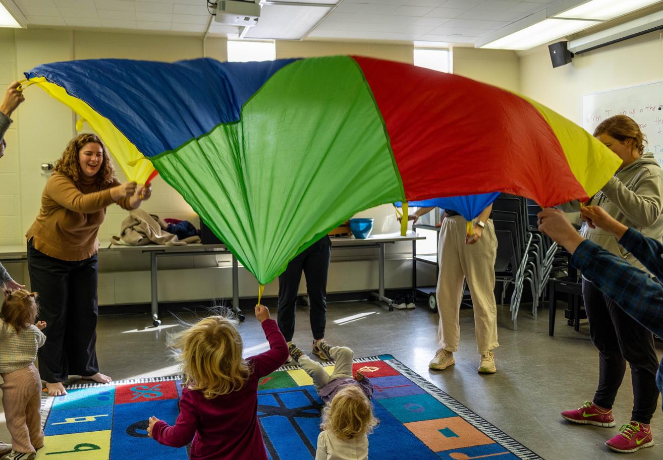 Adults and toddlers lift a rainbow parachute
