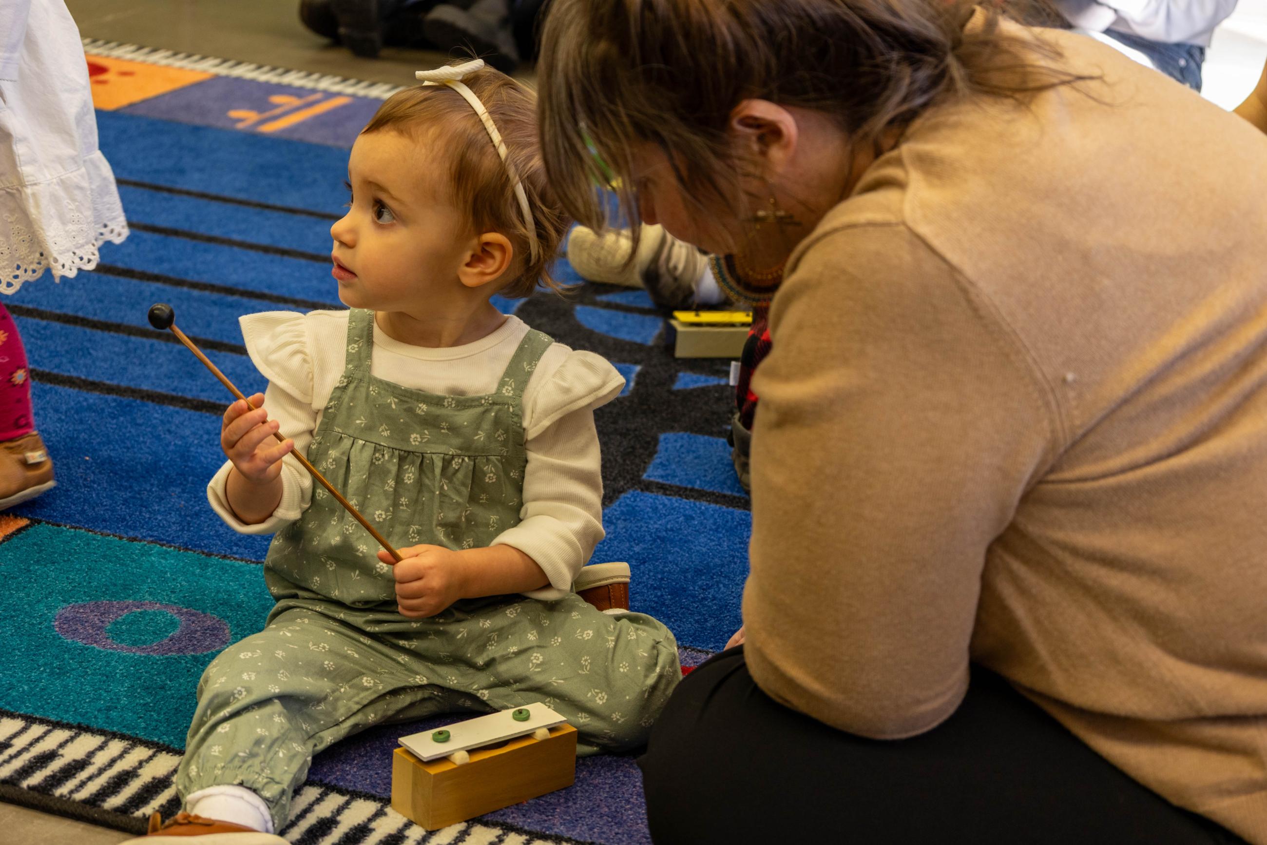 Toddler plays a tone block beside a caregiver.