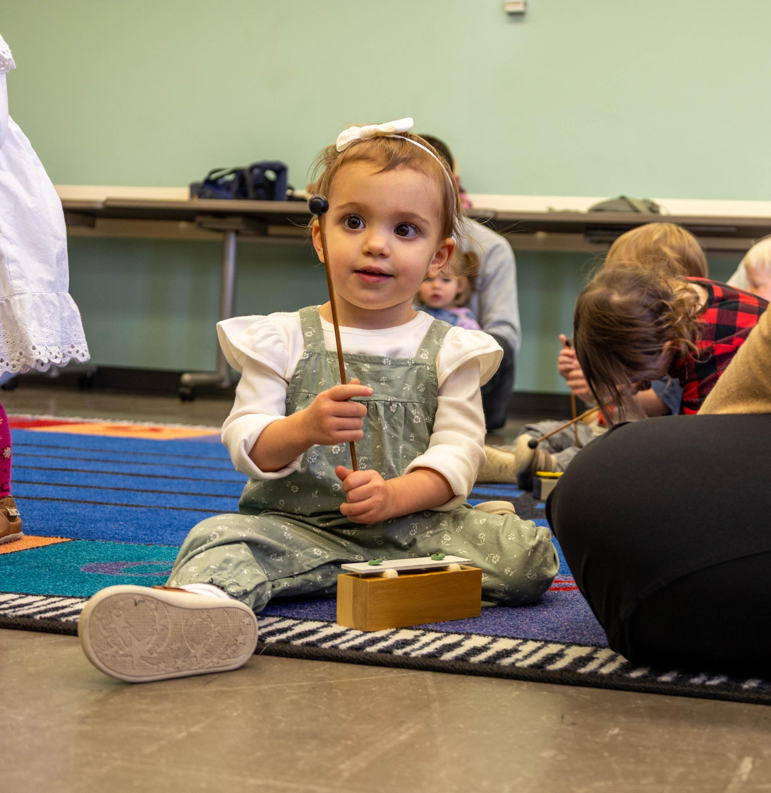 Toddler holds a mallet on a music rug.