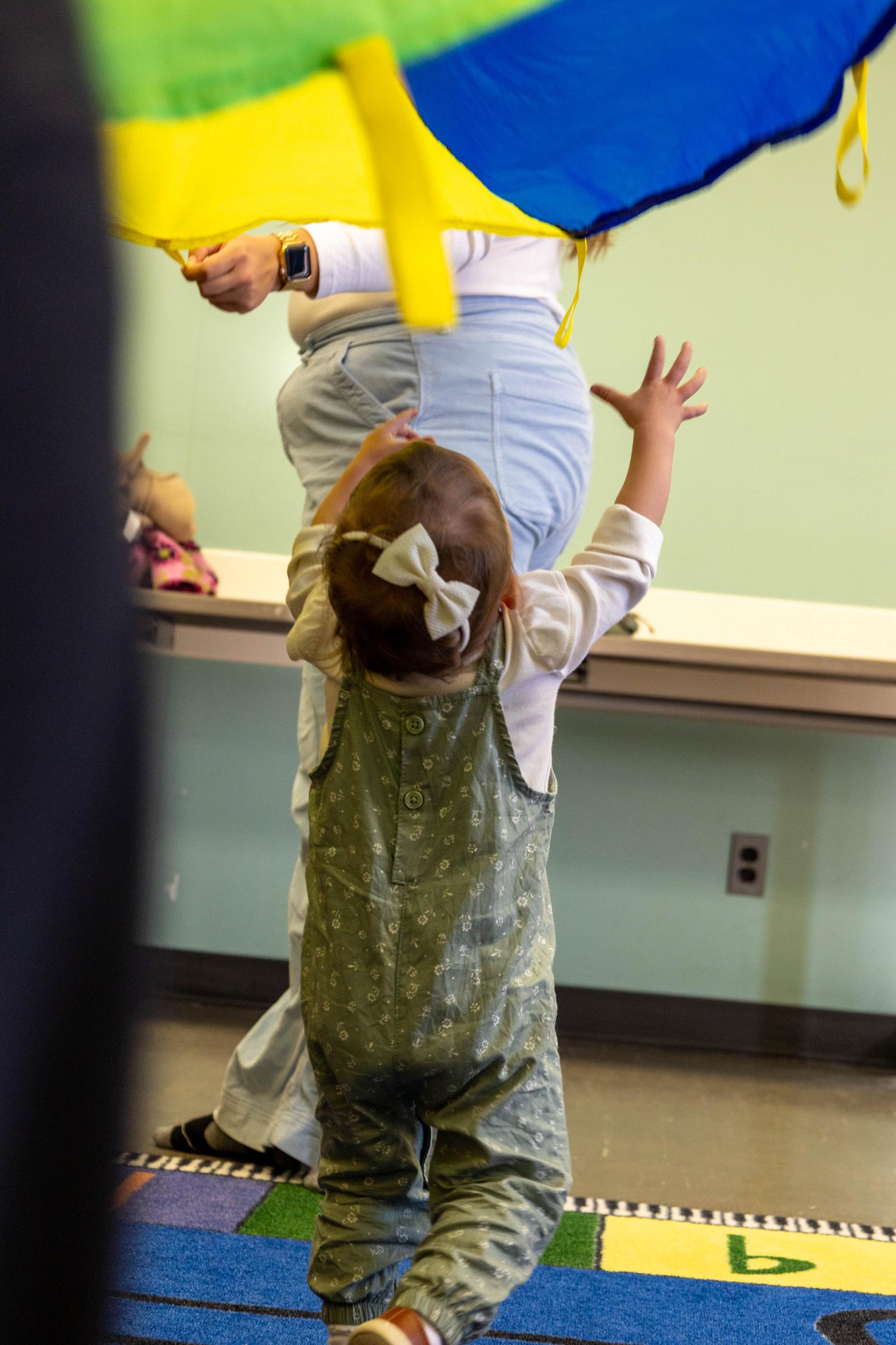 Toddler reaches up toward a rainbow parachute.