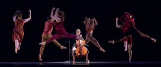 Person playing cello surrounded by dancers. 