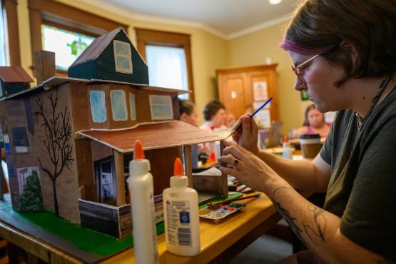Rea Klinger-Neviska painting a replica model of The Gathering Place house in Athens, Ohio