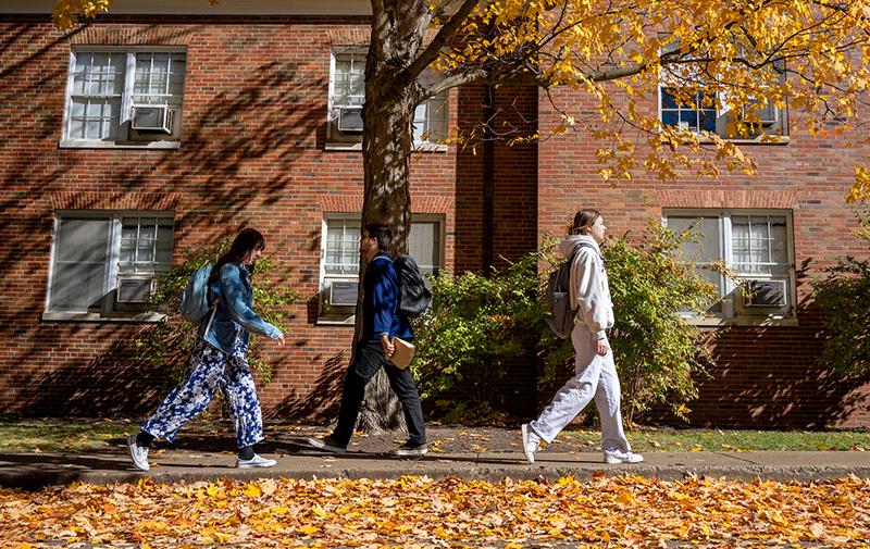 students walking through the fall leaves on campus