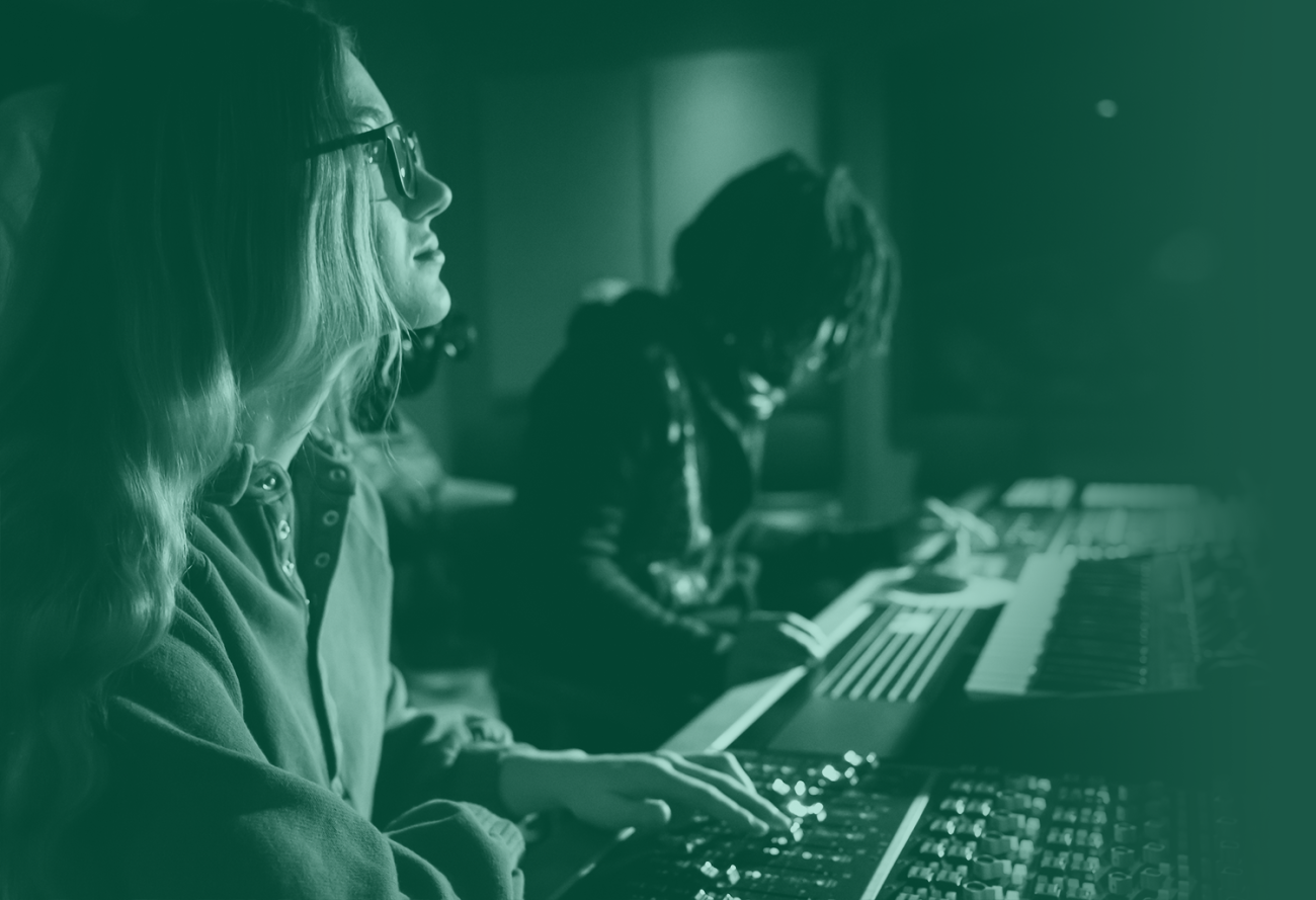 Two students working in a dark room adjusting knobs on a soundboard