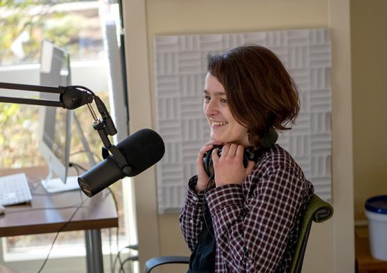 A woman sits in front of a microphone inside a sound studio