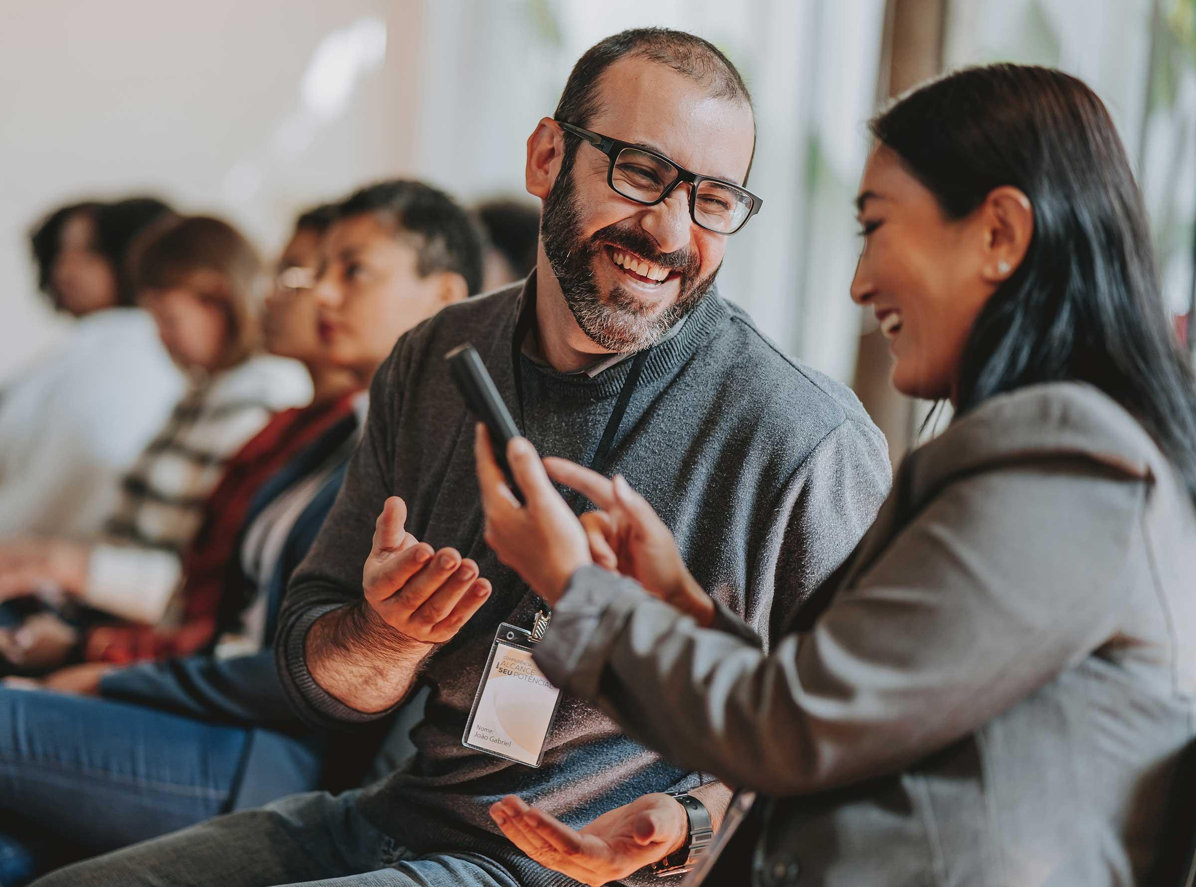 Man and woman smiling at phone while sitting together at event