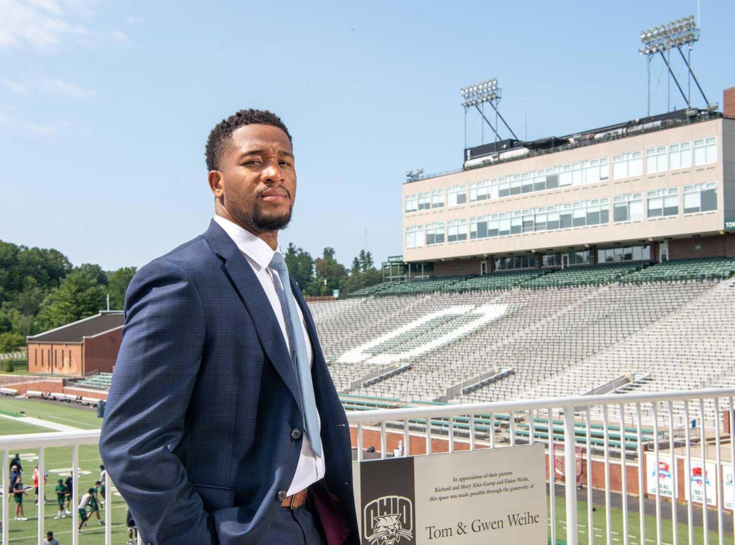 African American sports administrator in blue suit standing on bleachers beside football field