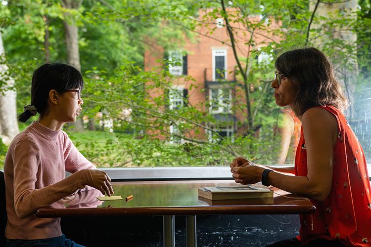 A student sits at a table while talking with their academic advisor