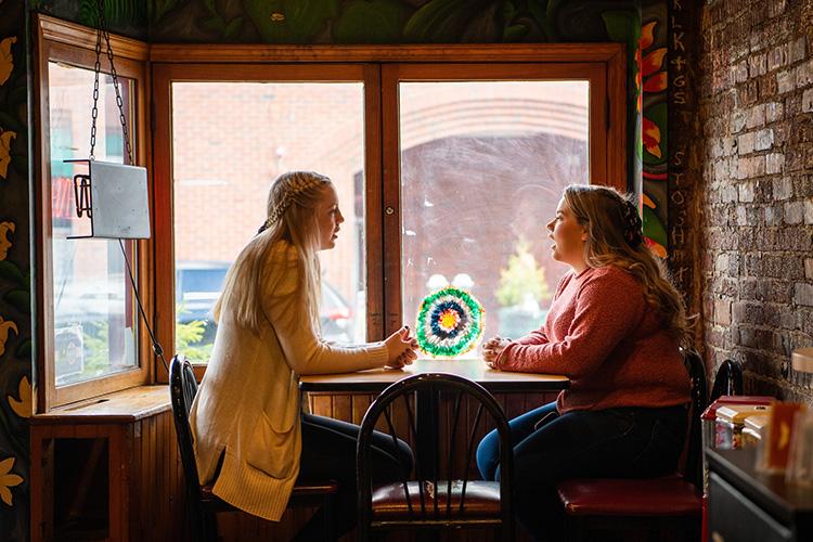 two female students sit at a table and talk