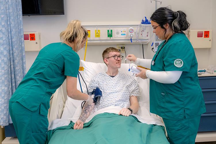 two nursing students taking the temperature and blood pressure levels of a patient