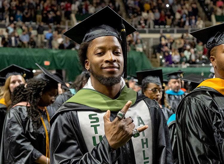 an OHIO graduate holds up a hand gesture while smiling for a photo