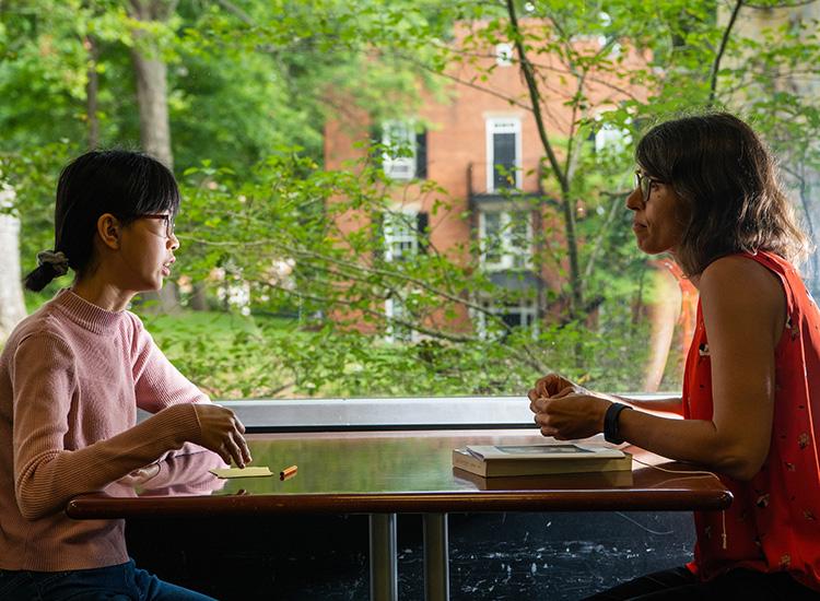 A student sits at a table while talking with their academic advisor