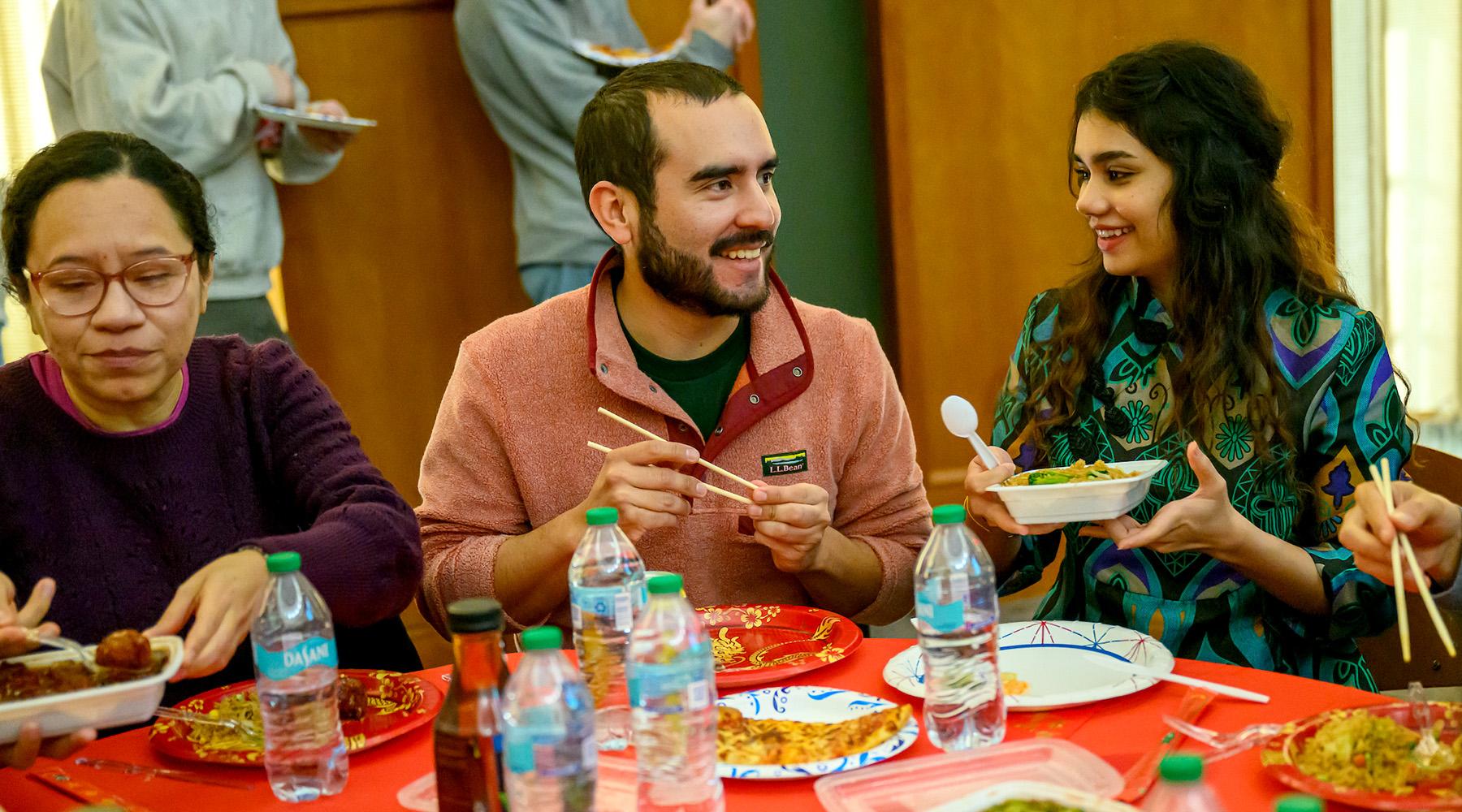 People sit at a table and eat from several different international foods