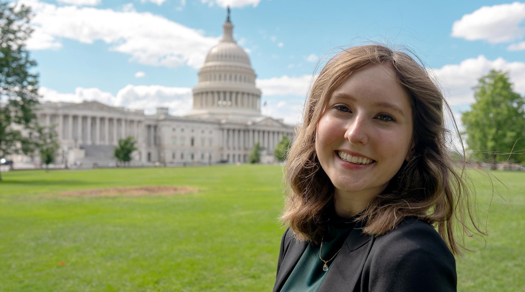 A female student poses for a photo with the Capitol Building in the background