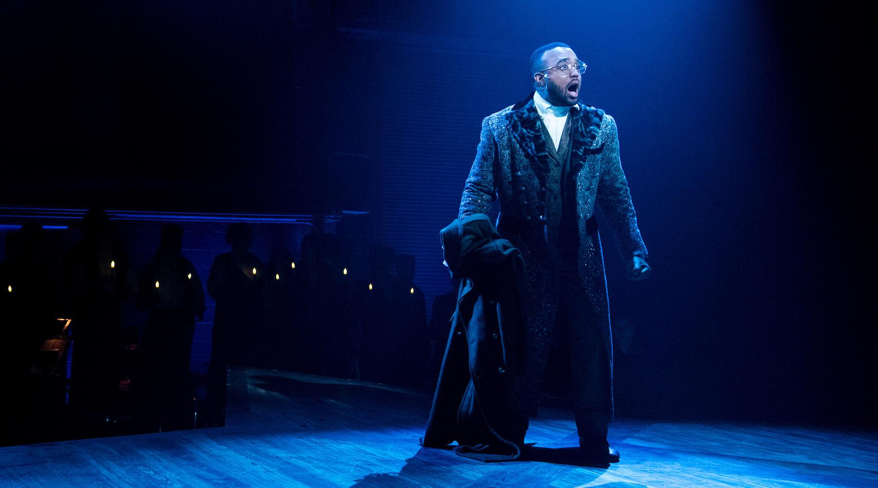 A man sings on stage in a dark room beneath a strong blue light