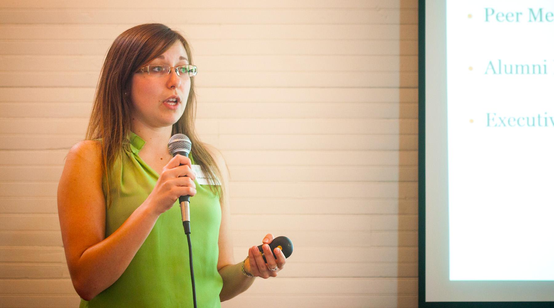 A woman stands with a microphone as she presents to a crowd of people