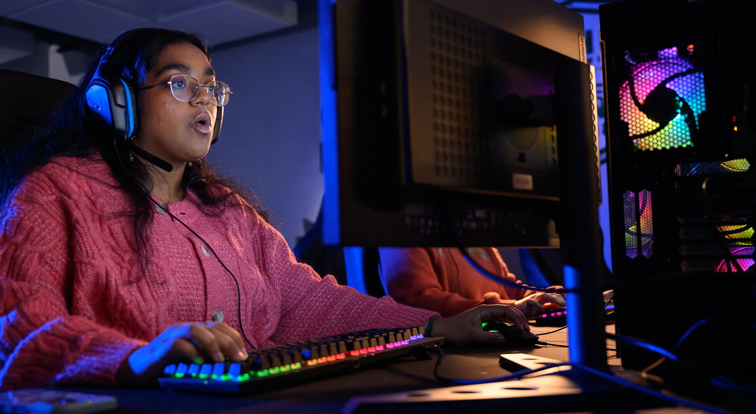 a female Esports student sits at a computer playing a game with a surprised look on her face