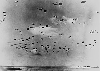 Black and white photograph of World War II planes and parachutes against a cloudy sky