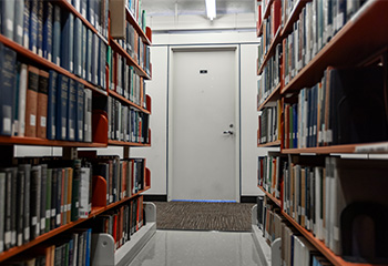 Image depicts a study carrel door at the end of two parallel shelving units filled with books.