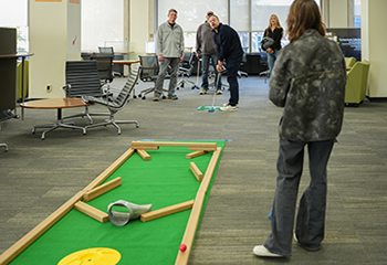 A young man lines up his shot on an Alden Open mini golf hole with a group of onlookers