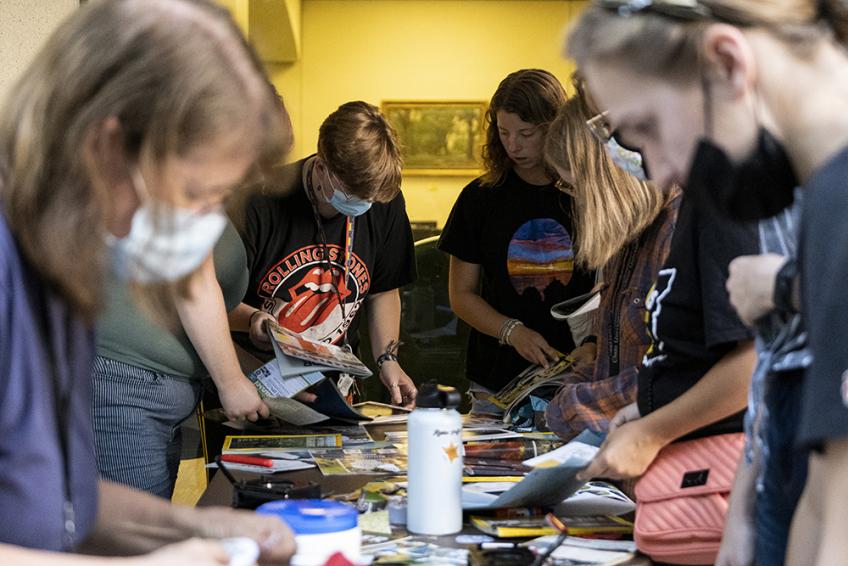 Several students stand around a table, paging through the magazines that cover the table