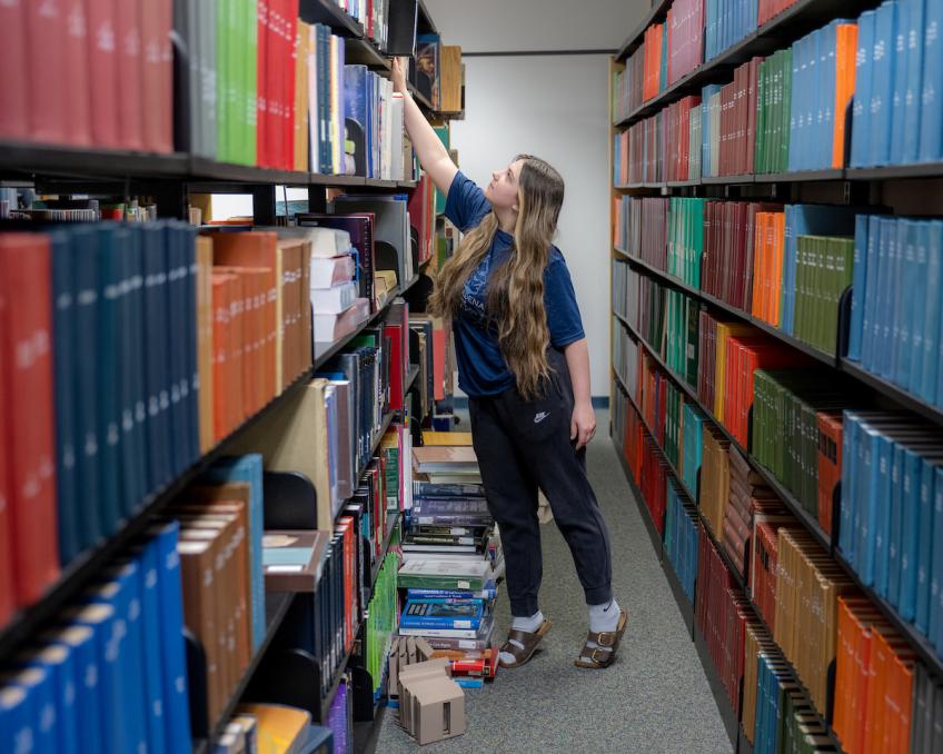 A student reaches for a book on a shelf in the Chillicothe Library stacks