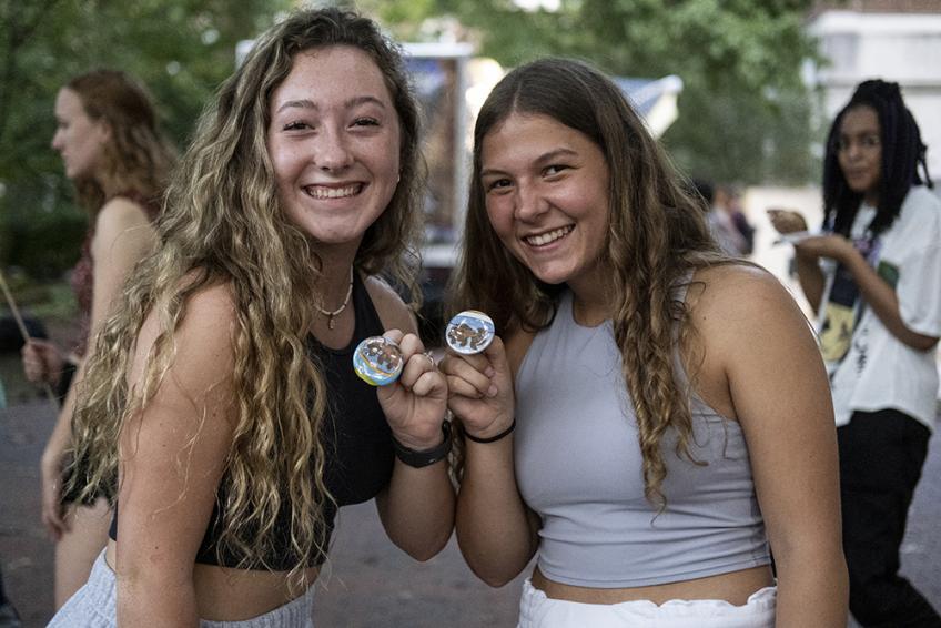 Two young women hold up buttons while smiling at the camera