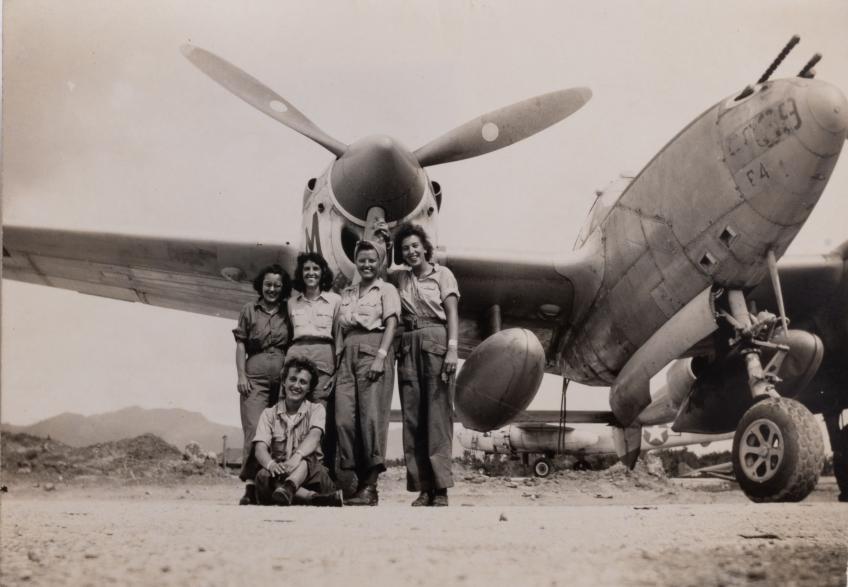 Black and white photograph of five women in military uniforms standing in front of a grounded World War II airplane