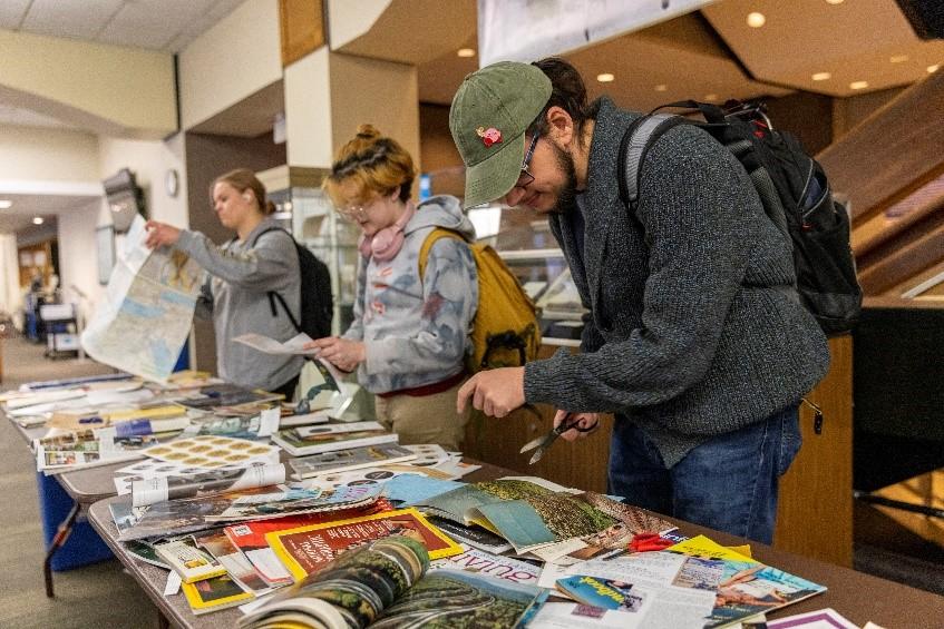 Three students browse a table covered with magazines