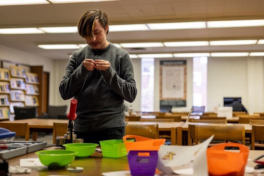 A young man looks at a table covered with button-making supplies