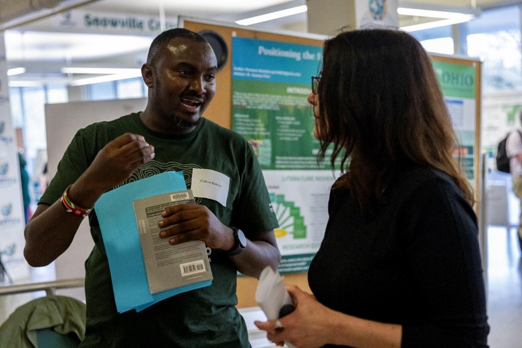Photo of 2024 Expo Awardee Collins Ketere talking about his research with library dead Janet Hulm
