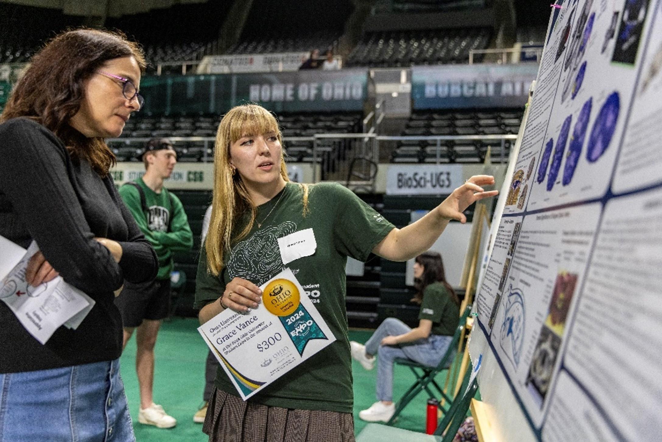 Photo of 2024 Expo awardee showing her poster to library dean Janet Hulm