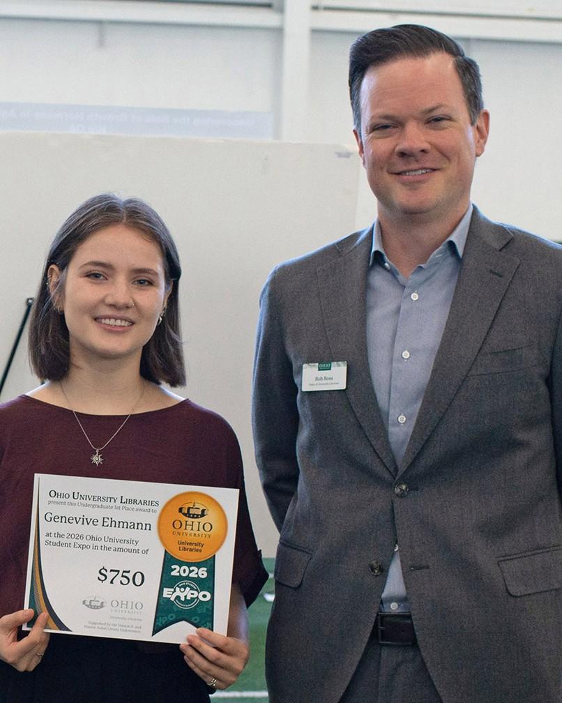 Person stands holding award certificate in front of their research poster. Tall man in grey suit stands next to them.