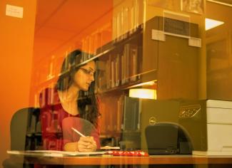 A graduate student writes and works on a laptop in the library