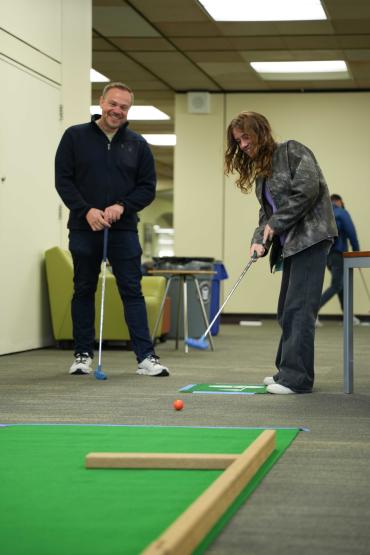 Sophomore Addison Barry putts a red golf ball with a blue putter while her father Sean watches at the Alden Open event