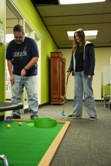 Father Chris Hansen lines up his mini golf shot on the 5th floor while his daughter, Senior Acadia Hansen, watches