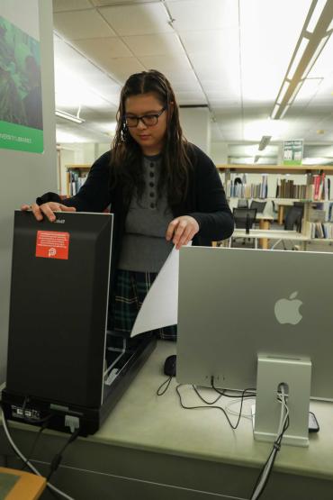 An Alden Library staff member opens a flat-bed scanner at a Mac computer station to scan a sheet of paper