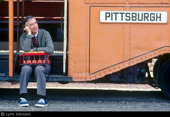 Fred Rogers holds Neighborhood Trolley and looks to side on Pittsburgh trolley steps