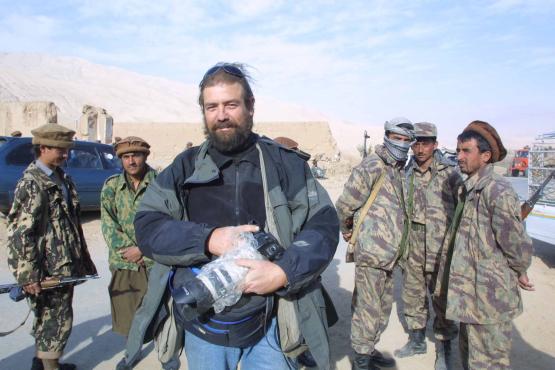 Len Vaughn-Lahman, on assignment in the Middle East, holding a camera with group of soldiers behind him, unknown location, circa 2001-2003.