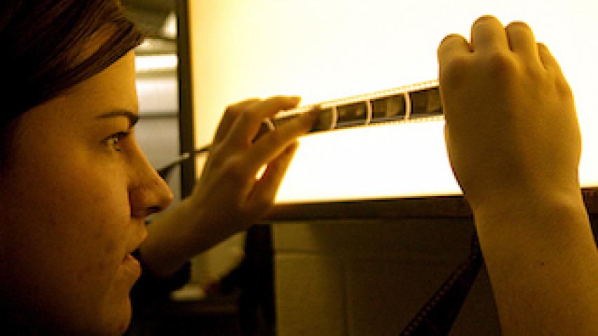 A woman holds a strip of photographic film against a lightbox