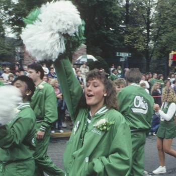 A cheerleader in a tracksuit lifts a pompom at 2021 Homecoming