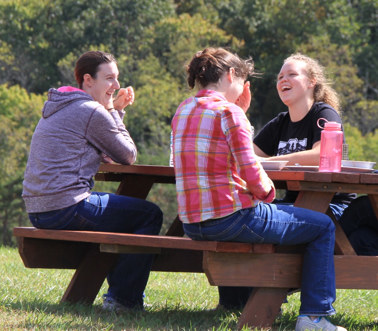 Three students sit at a picnic table outside and laugh
