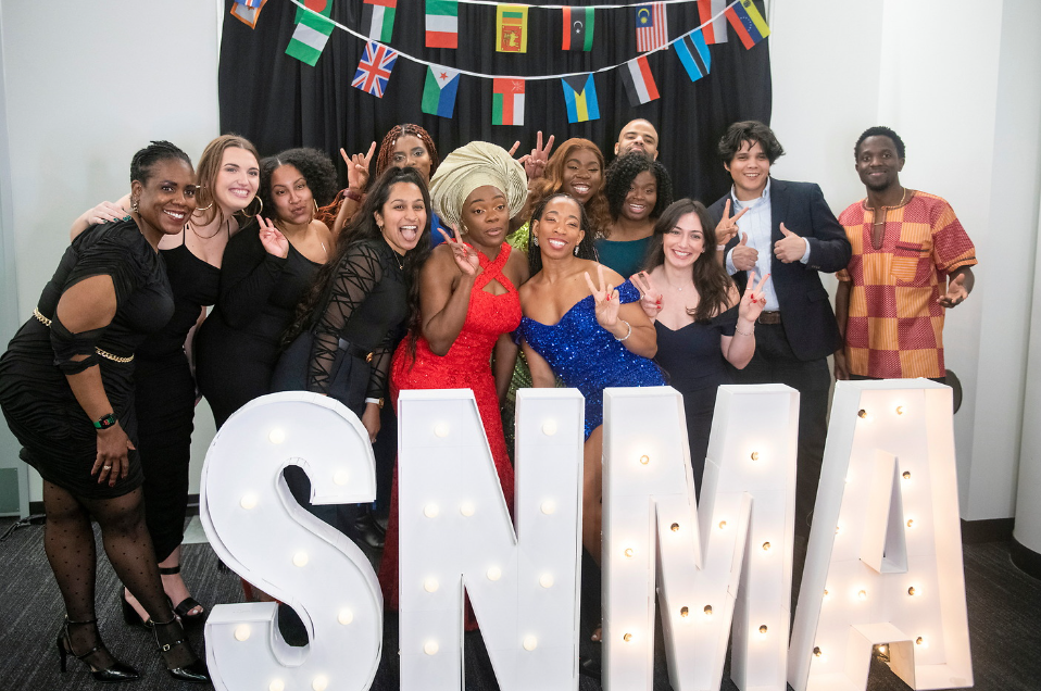 A group of Heritage College students pose for a photo behind a SNMA sign