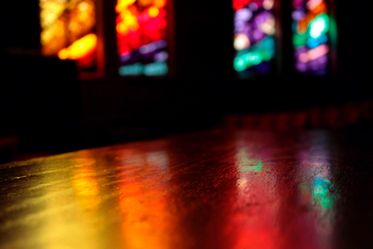 Light from a stained-glass window reflects off wood in a dark room