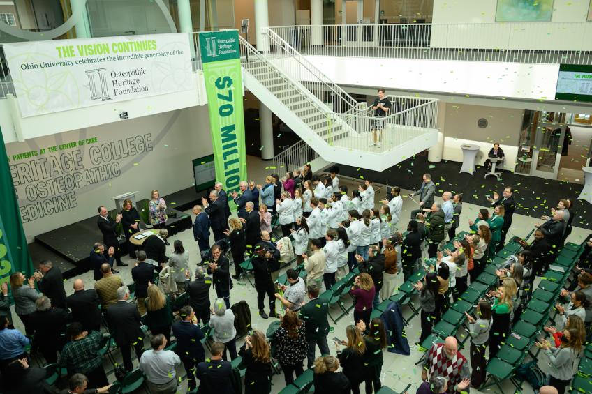 Crowd applauding in the Heritage Hall atrium during the January 2025 announcement of a $70 million gift from the Osteopathic Heritage Foundation, with celebratory confetti falling.