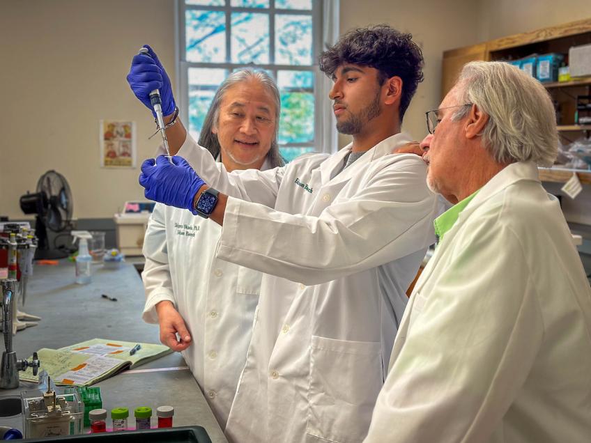 Student with pipette and two faculty working in lab.
