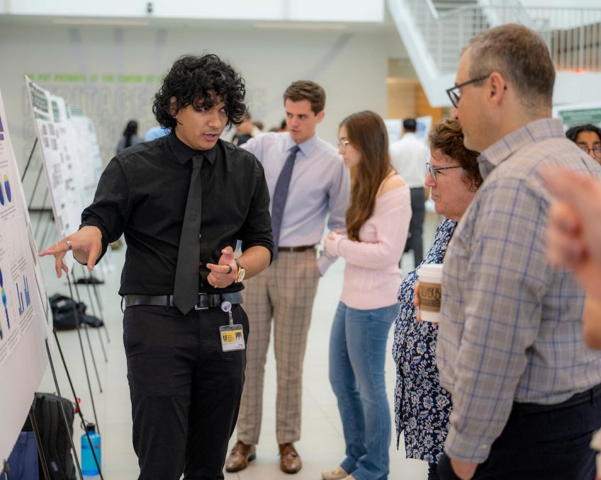 Student presenting a research poster to onlookers
