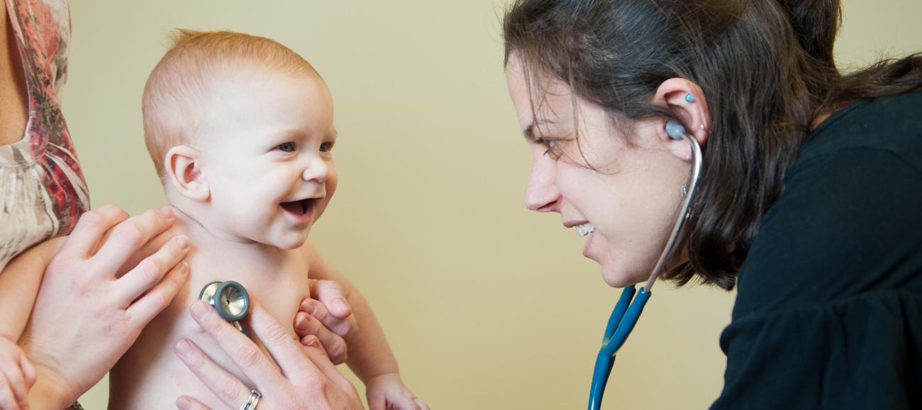 A medical student uses a stethoscope to listen to a smiling babies chest
